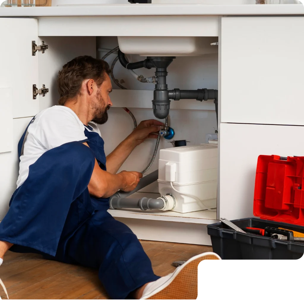 Professional plumber inspecting plumbing connections beneath a kitchen sink.